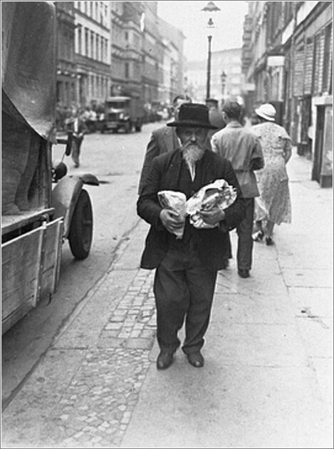 A Jewish man carrying two bags walks down the main commerical street of the Berlin Jewish quarter